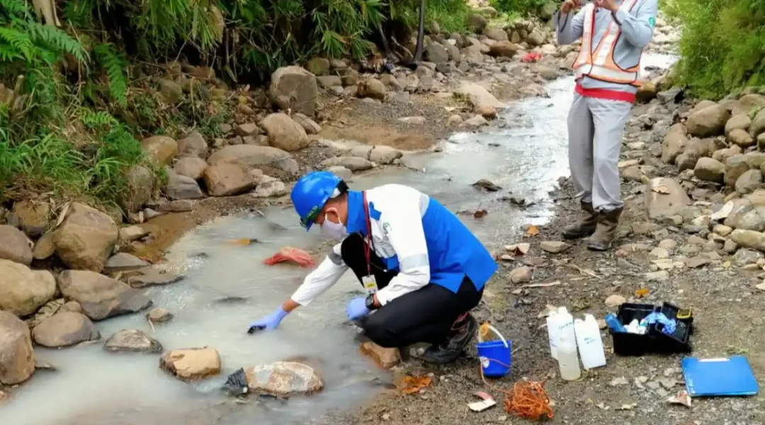 Foto petugas melakukan sampling air permukaan di pinggir sungai